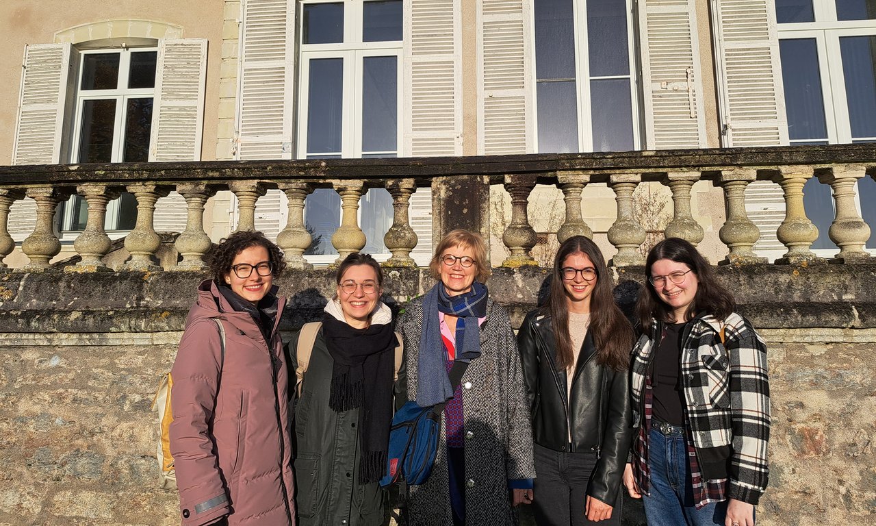 Gruppenfoto von fünf Personen im Freien in einer Stadt, im Hintergrund Fenster eines Gebäudes und ein Geländer.