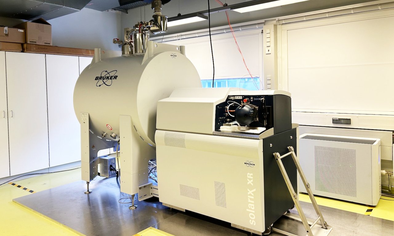 A large apparatus with a cylindrical part and a cubic part standing in the middle of a large, otherwise largely empty laboratory room