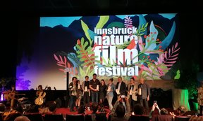 Siegerehrung bei einem Filmfestival mit vielen Menschen auf einer Bühne die Preise in der Hand halten