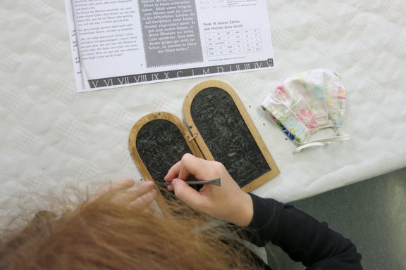 Ein Kind schreibt auf einem Wachstäfelchen