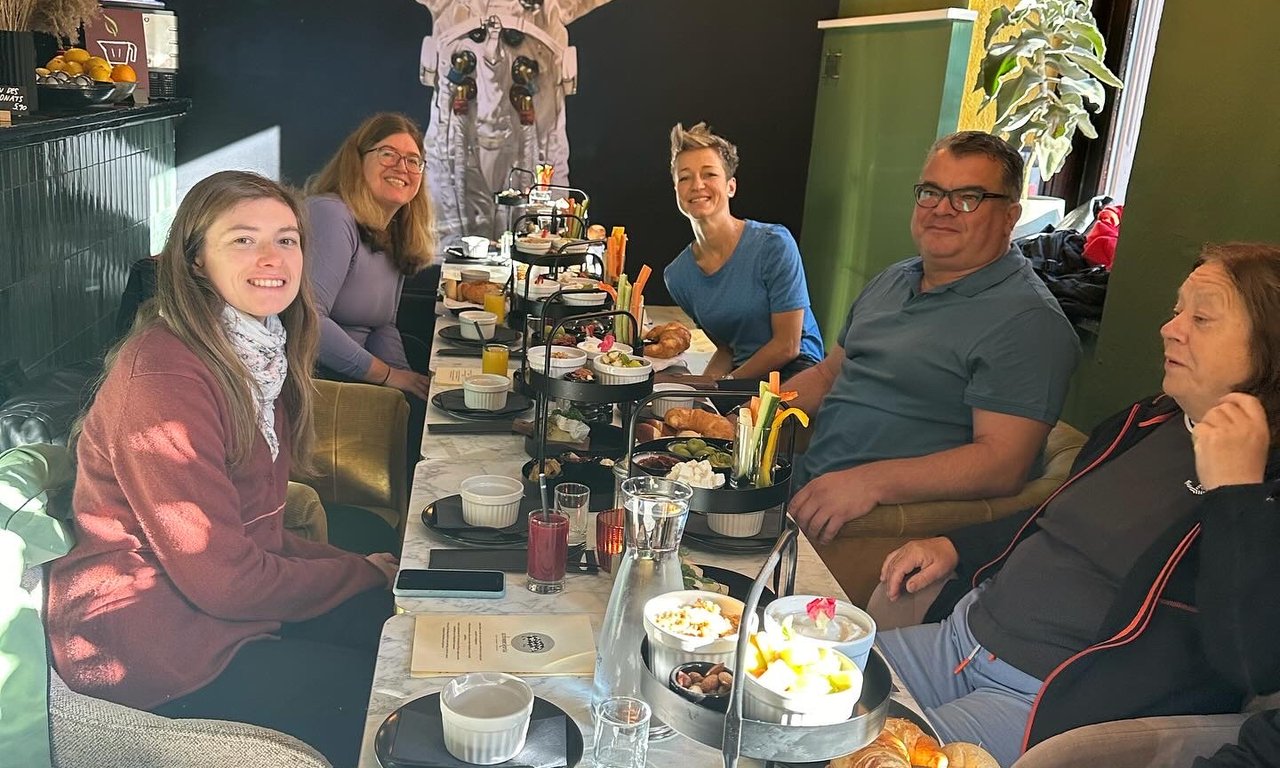 sechs Personen sitzen an einem Tisch, auf dem ein Frühstück steht