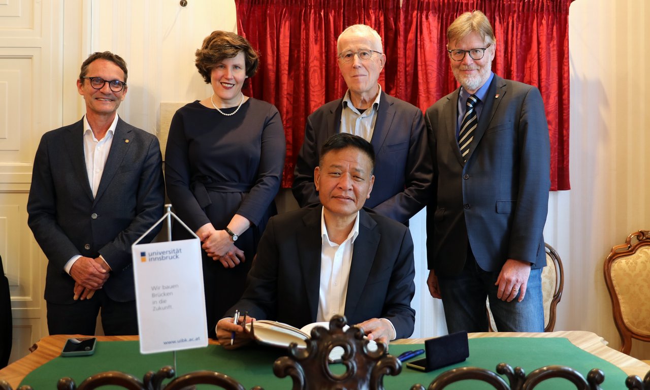 Gruppenfoto mit fünf Personen, ein Mann sitzt an einem Schreibtisch und schreibt in ein Buch.