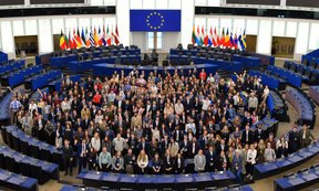 A bird's-eye view of the European Parliament's plenary chamber, showing a large group of young people looking up.