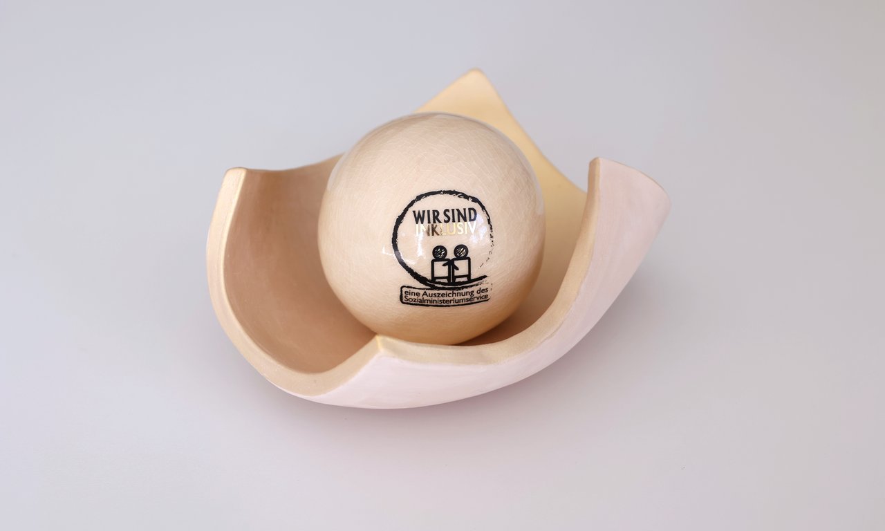 Die Auszeichnung für Inklusion, eine getöpferte Kugel in einer Schale in beige, auf einem weißen Tisch
