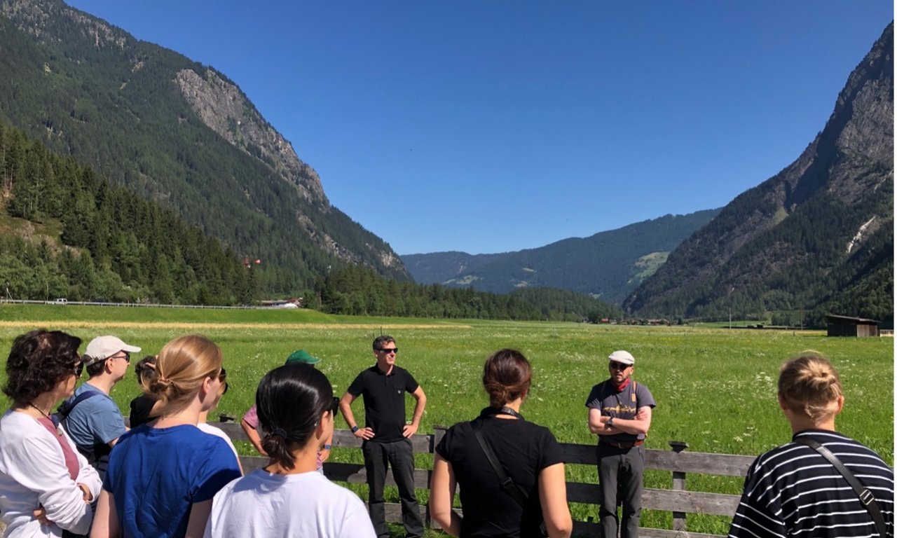 Mehrere Personen stehen mit dem Rücken zur Kamera vor einem Feld im Ötztal