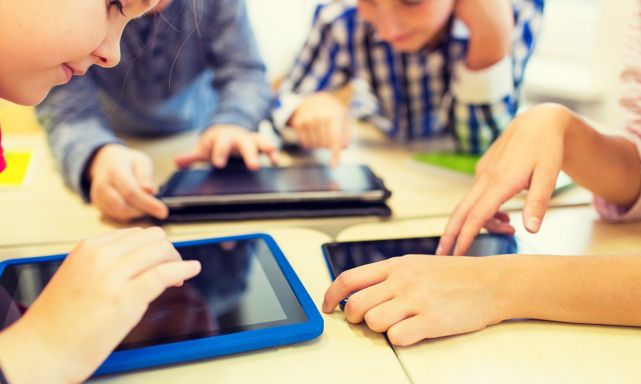Kinder sitzen vor Tablets an einem Tisch.