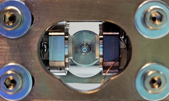 Metallischer Block mit einem Loch in der Mitte in dem zwei Spiegel und im Zentrum ein kleiner Zylinder zu sehen sind.