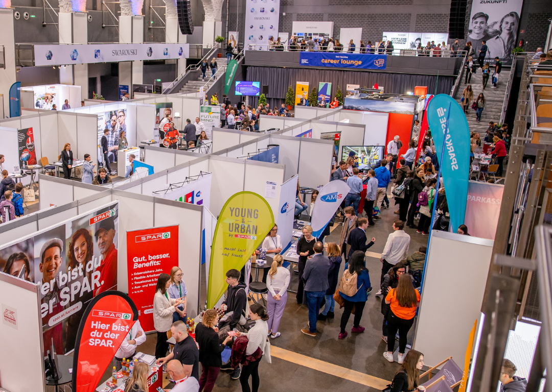 Blick auf eine Halle mit zahlreichen Messeständen  und vielen Menschen