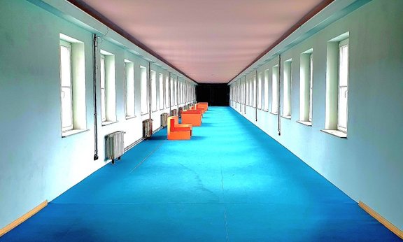 Ein langer Flur mit türkisfarbenem Teppich und orangenen Sesseln