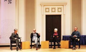 Foto einer Podiumsdiskussion: Vier Personen sitzen auf Stühlen auf der Bühne in der Aula der Universität