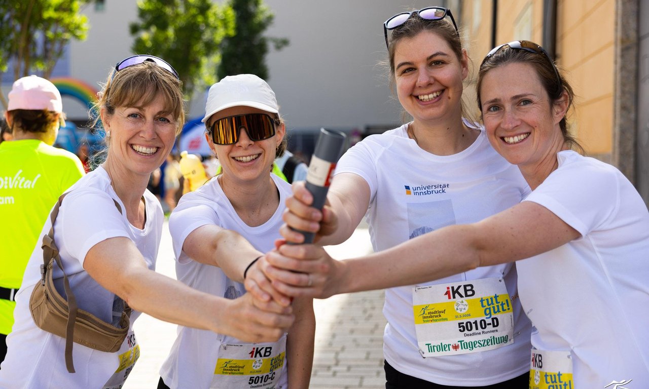 Vier Frauen im Sportoutfit halten gemeinsam einen Staffelstab.