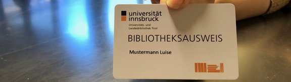 Das Bild zeigt eine Hand die einen Bibliotheksausweis der ULB-Tirol hält.