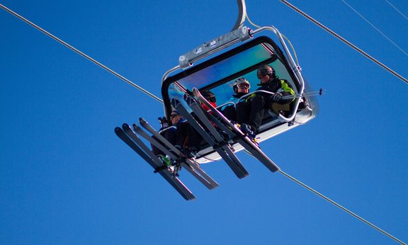 Blick von unten auf eine Gondel mit vier Skifahrern gegen den blauen Himmel