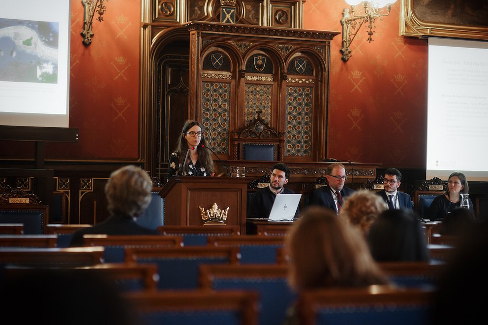 Frau an Rednerpult in einem prunkvollen Saal
