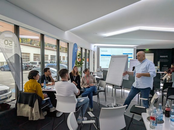 zeigt Studierende im kreis sitzend und vor ihnen steht ein Swarco-Expterte und erklärt ihnen etwas