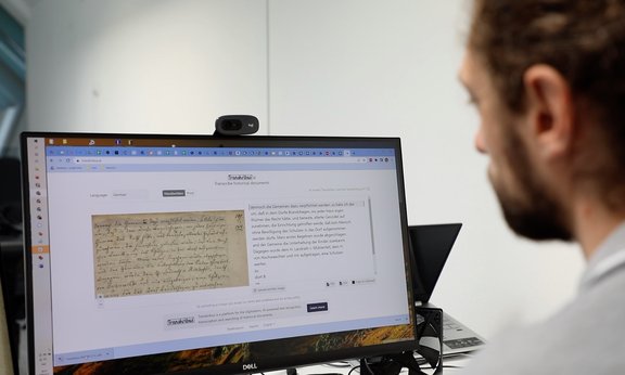 A man sits in front of a screen showing historical documents.