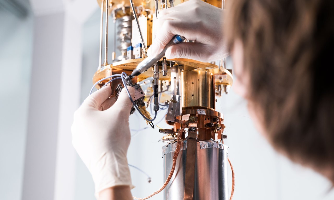 Two hands in white gloves assemble a brass-colored device.