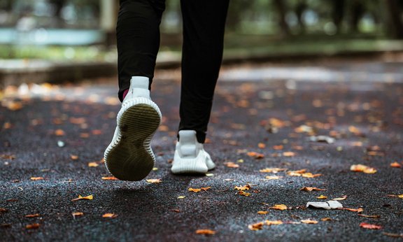 Zwei Beine mit weißen Turnschuhen auf einem Waldboden