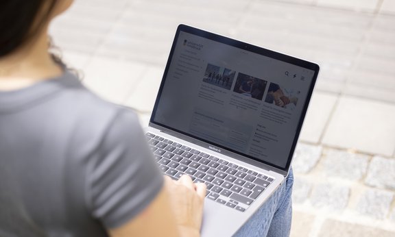 Student sitzt mit Laptop vor Agnes-Heller-Haus