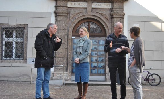 Vier Personen vor dem Gebäude der Theologie, ins Gespräch vertieft
