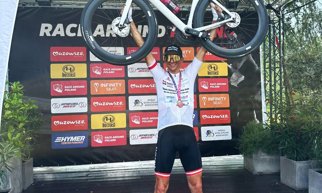 Ein Sportler auf einem Podium hält sein Fahrrad in die Höhe.