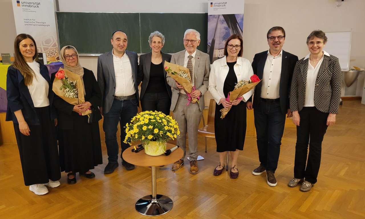 Zu sehen sind Martina Kraml, Matthias Scharer und Hamideh Mohagheghi zusammen mit Mitgliedern der Fachbereiche der Katholischen und Islamischen Religionspädagogik. Sie befinden sich in einem Hörsaal. Sie halten Blumen in der Hand.