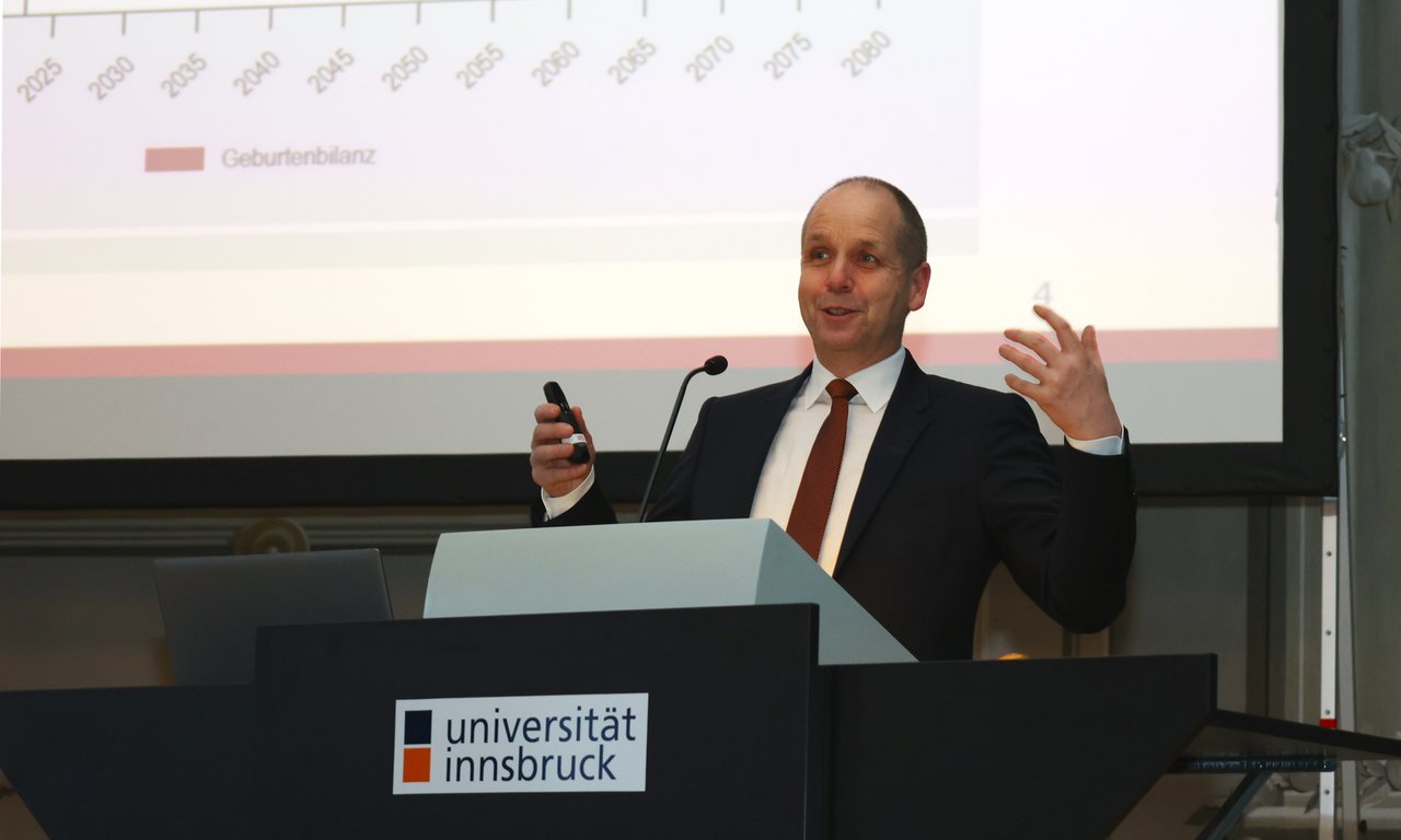 Eine Person steht an einem Rednerpult auf dem der Schriftzug "Universität Innsbruck" steht.
