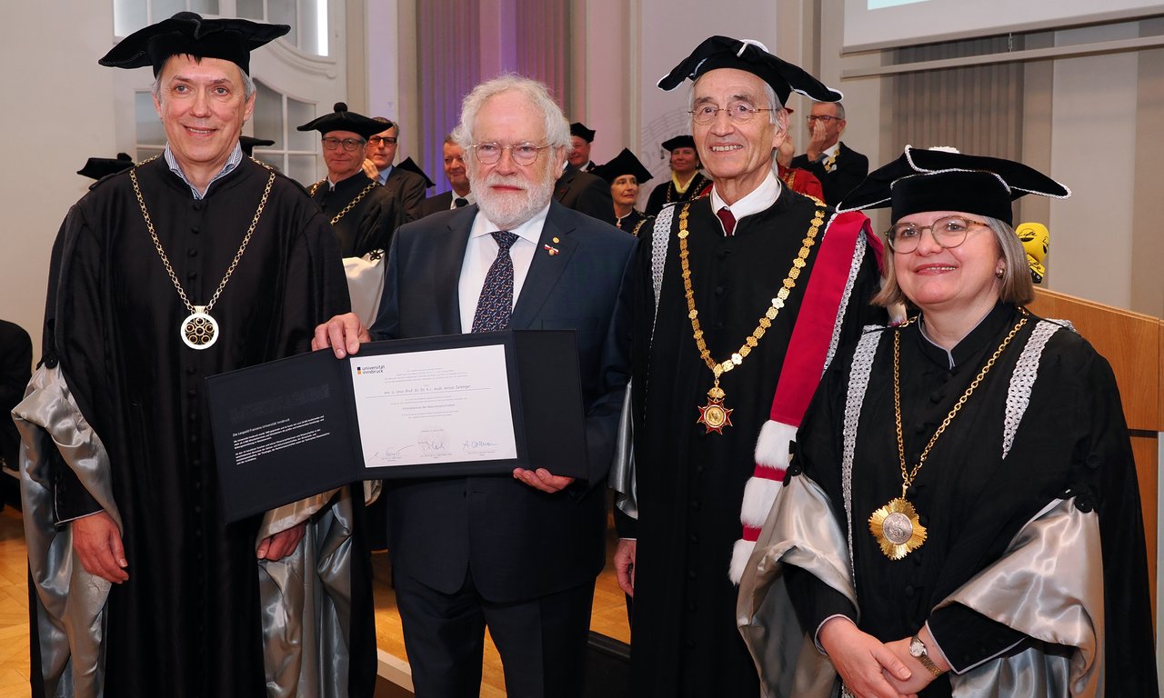 Three men and one woman stand together for a group photo in the auditorium, one of the men holds a certificate.