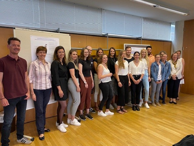 15 Studierende stehen in einem Seminarraum