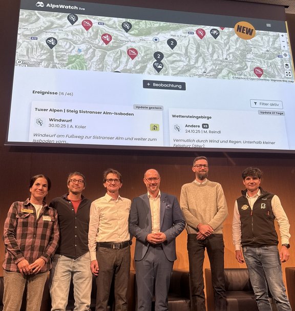 Mehrere Personen auf einer Bühne, dahinter eine Leinwand.