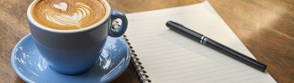 Kaffeetasse und ein Schreibblock mit einem Stift