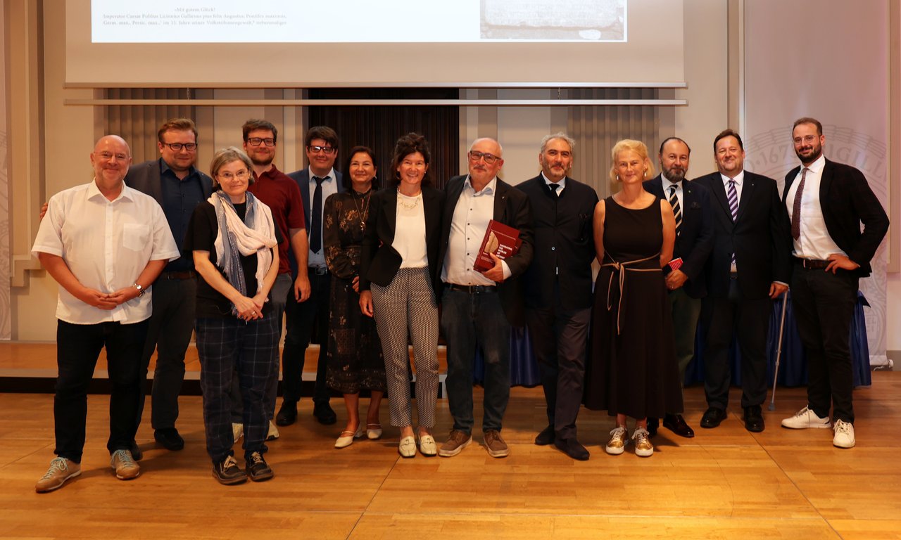 Zahlreiche Personen stehen auf einem Podium und blicken in die Kamera