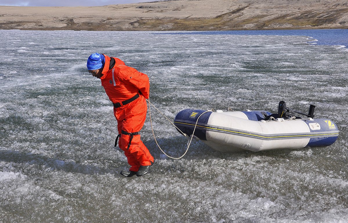 Eine Person in orangem Overall zieht ein Schlauchboot für eine Eisfläche auf einem See