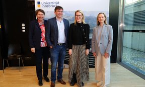 Vier Personen stehen in einer Reihe vor einer Pressewand mit dem Logo der Universität Innsbruck.