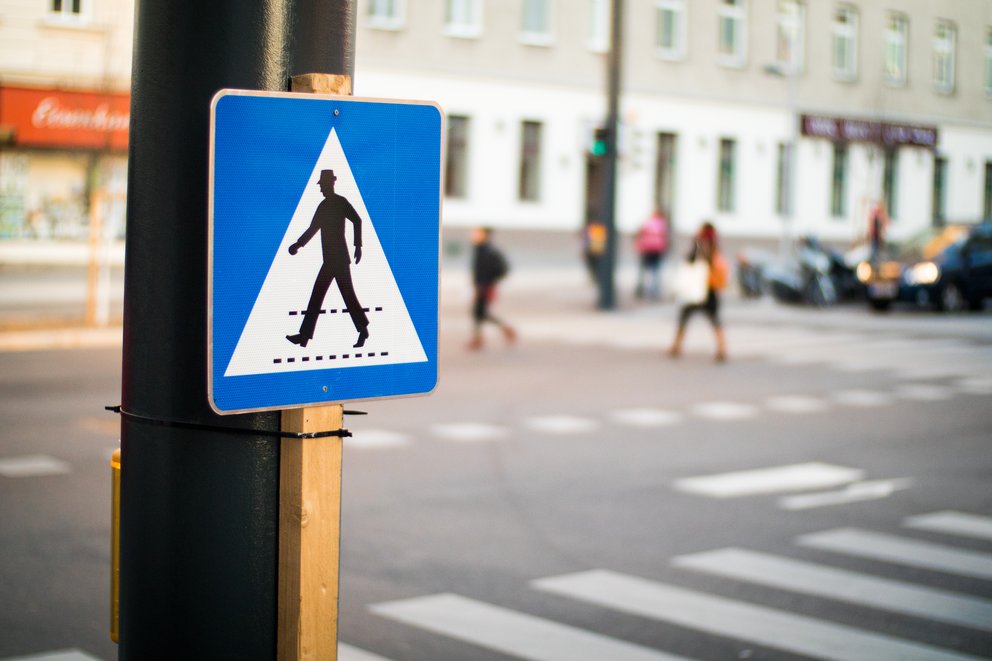 Verkehrsschild Fußgängerübergang mit Zebrastreifen und Fußgänger im unscharfen Hintergrund