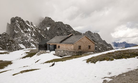 Hütte vor Bergspitzen im Schnee