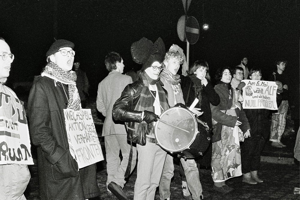 Ein SW-Foto von mehreren Menschen, die auf einer Demonstration in einer Reihe gehen.