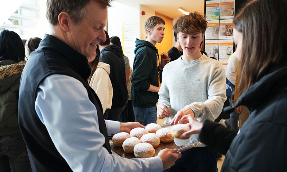 Person verteilt Krapfen an Schüler:innen