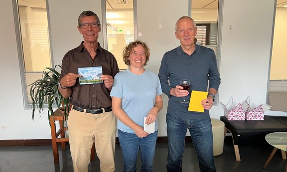 Auf dem Bild zu sehen sind drei Personen. Sie halten eine Karte in der Hand und freuen sich.