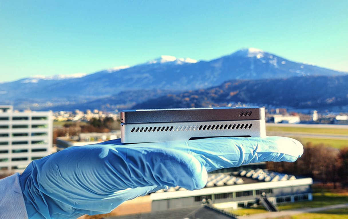 Eine Hand hält eine kleine Sequenzierungsmaschine vor Bergkulisse in die Höhe