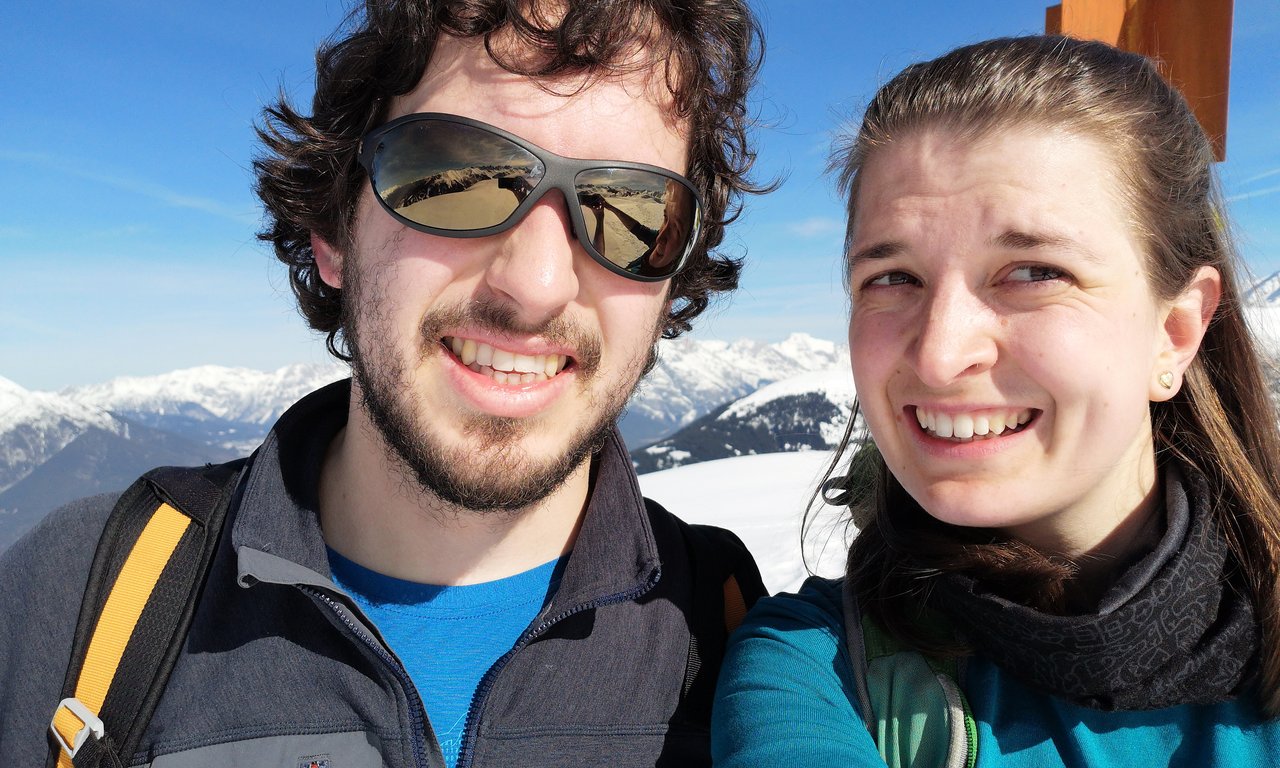 Zwei Personen lachen in die Kamera. Im Hintergrund Berge