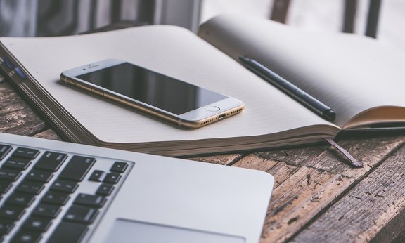 Laptop, Handy und Linienblock auf einem Tisch