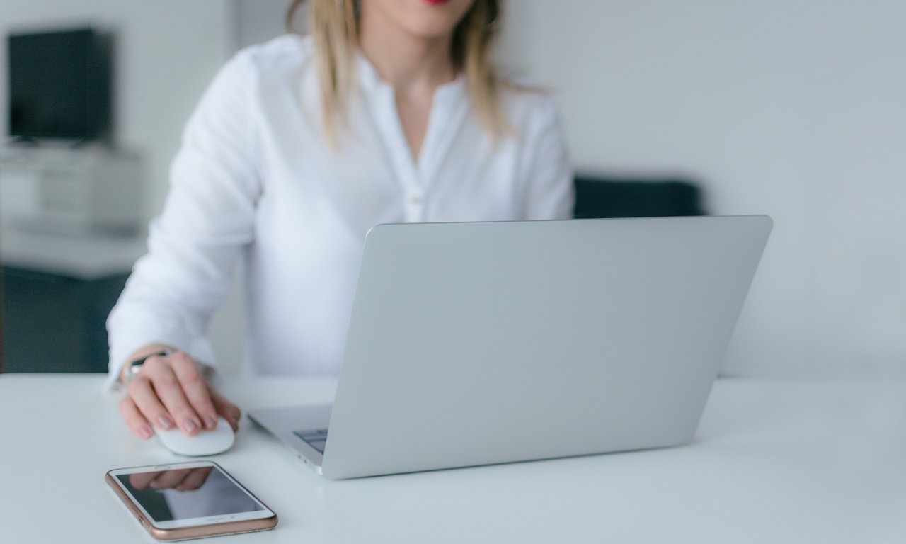 Frau sitzt an einem Laptop, neben ihr liegt ein Smartphone, sie hat Kopfhörer im Ohr