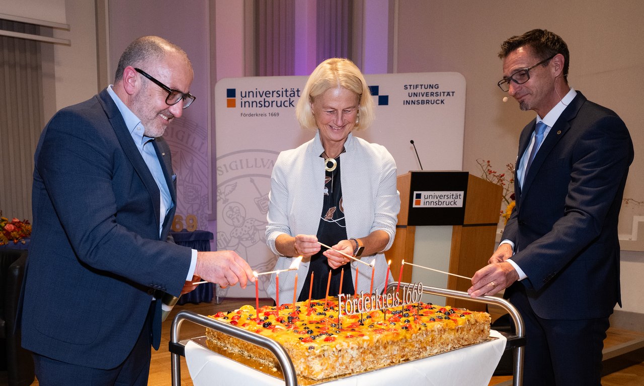 Drei Personen zünden gemeinsam Kerzen auf einer Torte an.