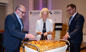 Drei Personen zünden gemeinsam Kerzen auf einer Torte an.