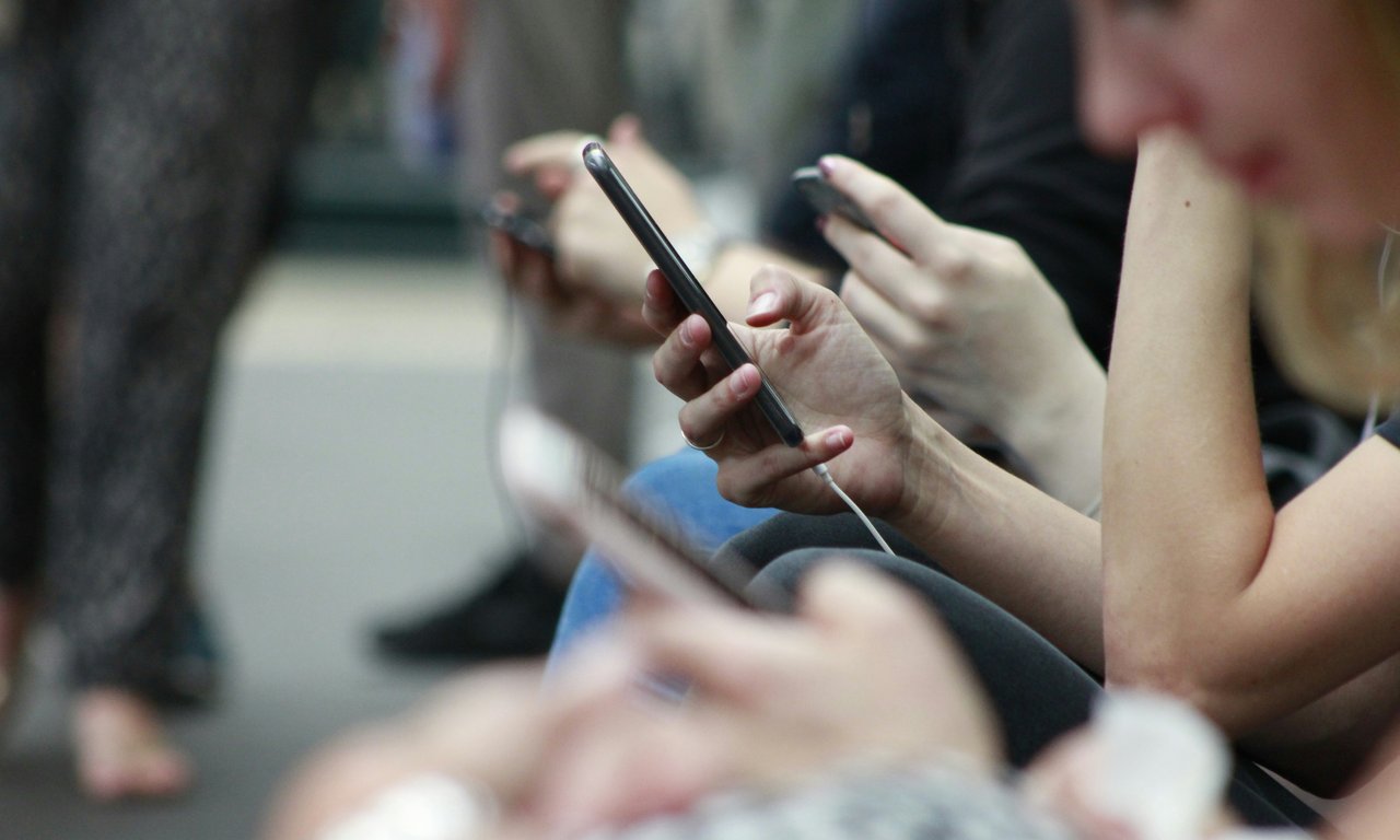 Nahaufnahme von mehreren Händen nebeneinander, die ein Smartphone halten.