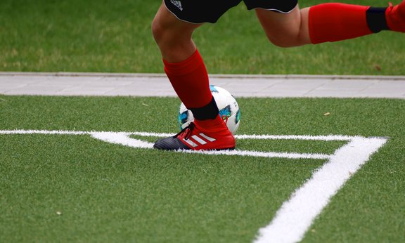 Jugador de fútbol durante el partido. Pronto da una patada al balón que tiene delante, sólo se le ven las piernas.