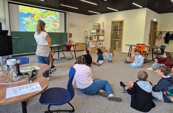 Kinder sitzen auf dem Boden und schauen zur Workshop-Leiterin