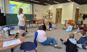 Kinder sitzen auf dem Boden und schauen zur Workshop-Leiterin