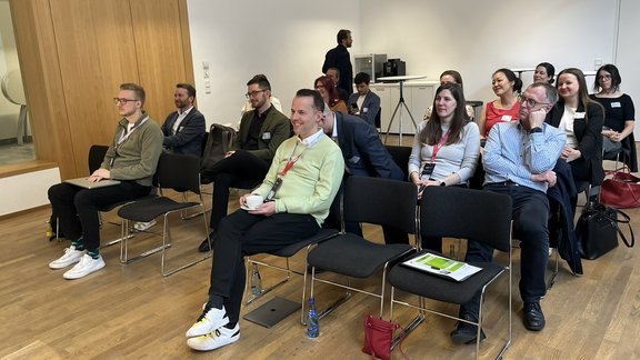 Blick in den Raum von vorn: die Teilnehmenden sitzen in Vortragsbestuhlung und hören zu.